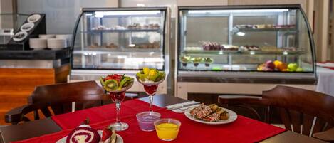 Una mesa de comedor con mantel rojo, diversos postres y un frutero.