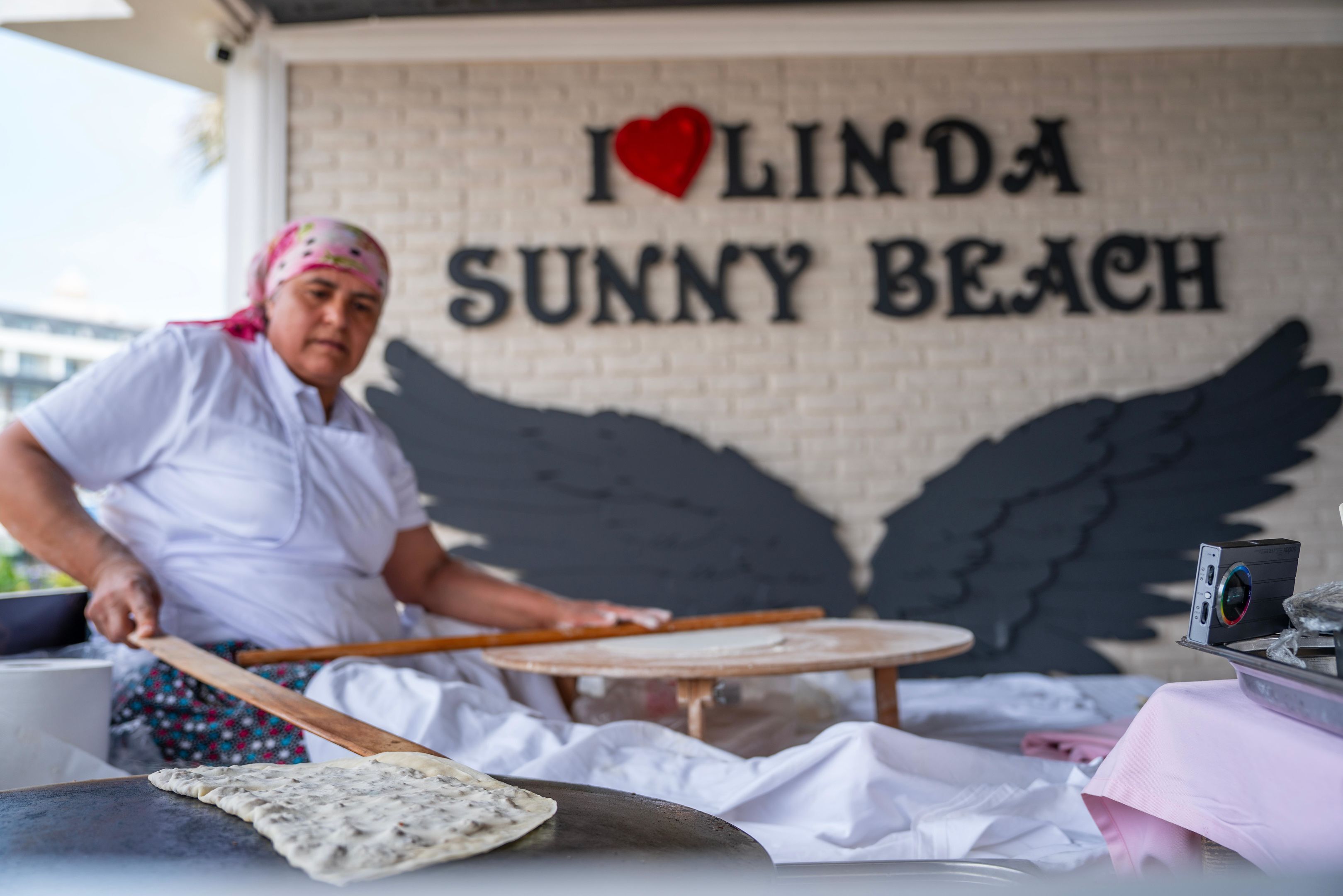 A person cooking on a portable stove with a sign in the background that reads "I ♥ LINDA SUNNY BEACH".