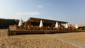 Restaurante à beira-mar com mesas ao ar livre e guarda-sóis.