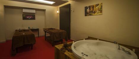 A bathroom with a large bathtub, a wooden bench, a table with towels, and a painting on the wall.