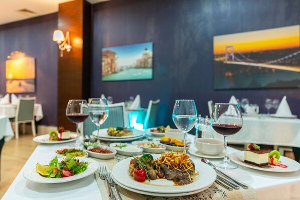 A restaurant with multiple dining tables set with plates of food, glasses of wine, and a view of a cityscape through the windows.