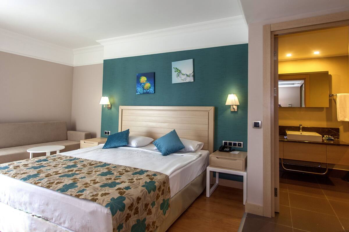 Camera d'albergo con un letto grande, comodini, un divano e un bagno con lavandino e specchio.