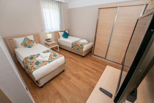 Une chambre d’hôtel avec deux lits, un plancher en bois, une télévision et une table de chevet avec une lampe.