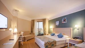 Quarto de hotel com duas camas, uma escrivaninha, uma cadeira, uma TV e uma varanda com cortinas.