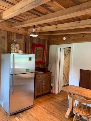 A kitchen with a stainless steel refrigerator, wooden cabinets, a wooden ceiling, and a door leading to another room.