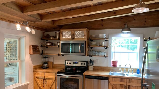 A compact kitchen with wooden cabinets, a microwave, a stove, and a dishwasher. - Remodeled French Country Style Cottage Close to Hiking Trails and Hot Springs (Hot Springs)