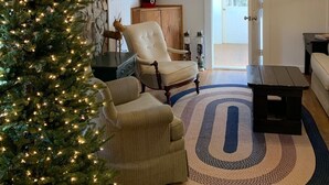 A cozy living room with a large Christmas tree, wooden beams on the ceiling, a fireplace, and a door leading outside. - Remodeled French Country Style Cottage Close to Hiking Trails and Hot Springs (Hot Springs)