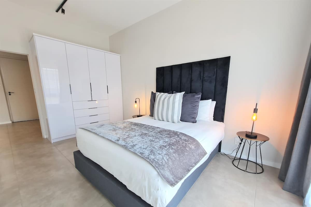 Een moderne slaapkamer met een groot bed, een garderobe en een nachtkastje met een lamp.