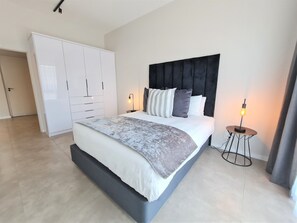 A modern bedroom with a large bed, a wardrobe, and a bedside table with a lamp. - MINT Apartments Greenside (Randburg)