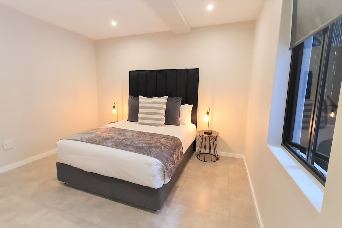 Een moderne slaapkamer met een bed, bedlampen, een raam en een stopcontact.