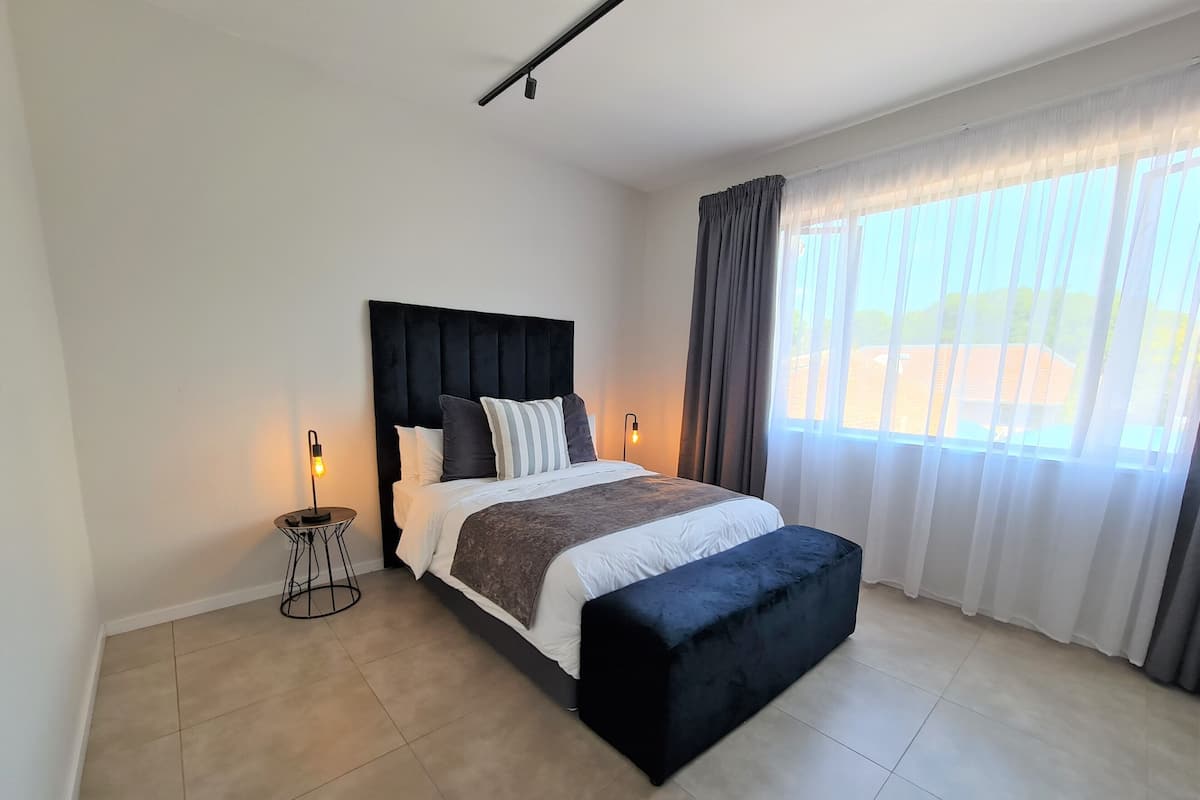 Een moderne slaapkamer met een groot bed, een nachtkastje en een raam met gordijnen.