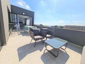 A modern outdoor balcony with a dining area, including a table and chairs, and a sofa. - MINT Apartments Greenside (Randburg)