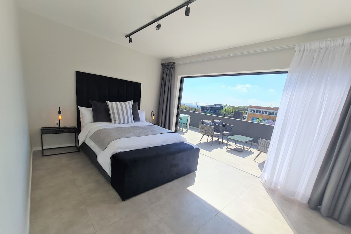 Een moderne slaapkamer met een groot bed, een nachtkastje met lamp en een balkon met tuinmeubilair.