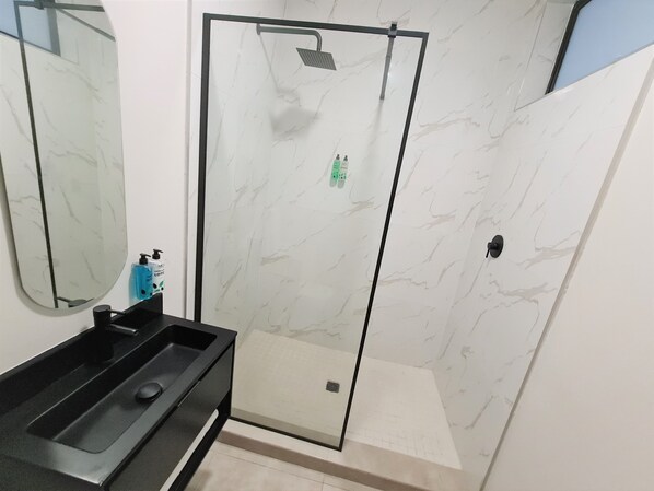 Un baño con ducha envuelta en cristal, tocador negro y espejo.