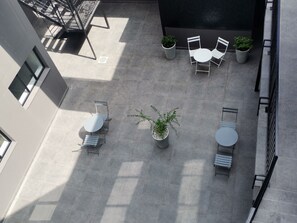 An outdoor patio area with a seating arrangement including two round tables and four chairs, surrounded by potted plants. - MINT Apartments Greenside (Randburg)