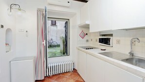 Eine kleine Küche mit weißen Schränken, einer Edelstahl-Spüle und einem Fenster mit Blick nach draußen.