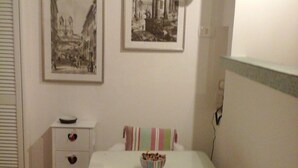 Ein kleiner Essbereich mit einem weißen Tisch und Stühlen, einem gestreiften Kissen sowie zwei gerahmten Bildern an der Wand.