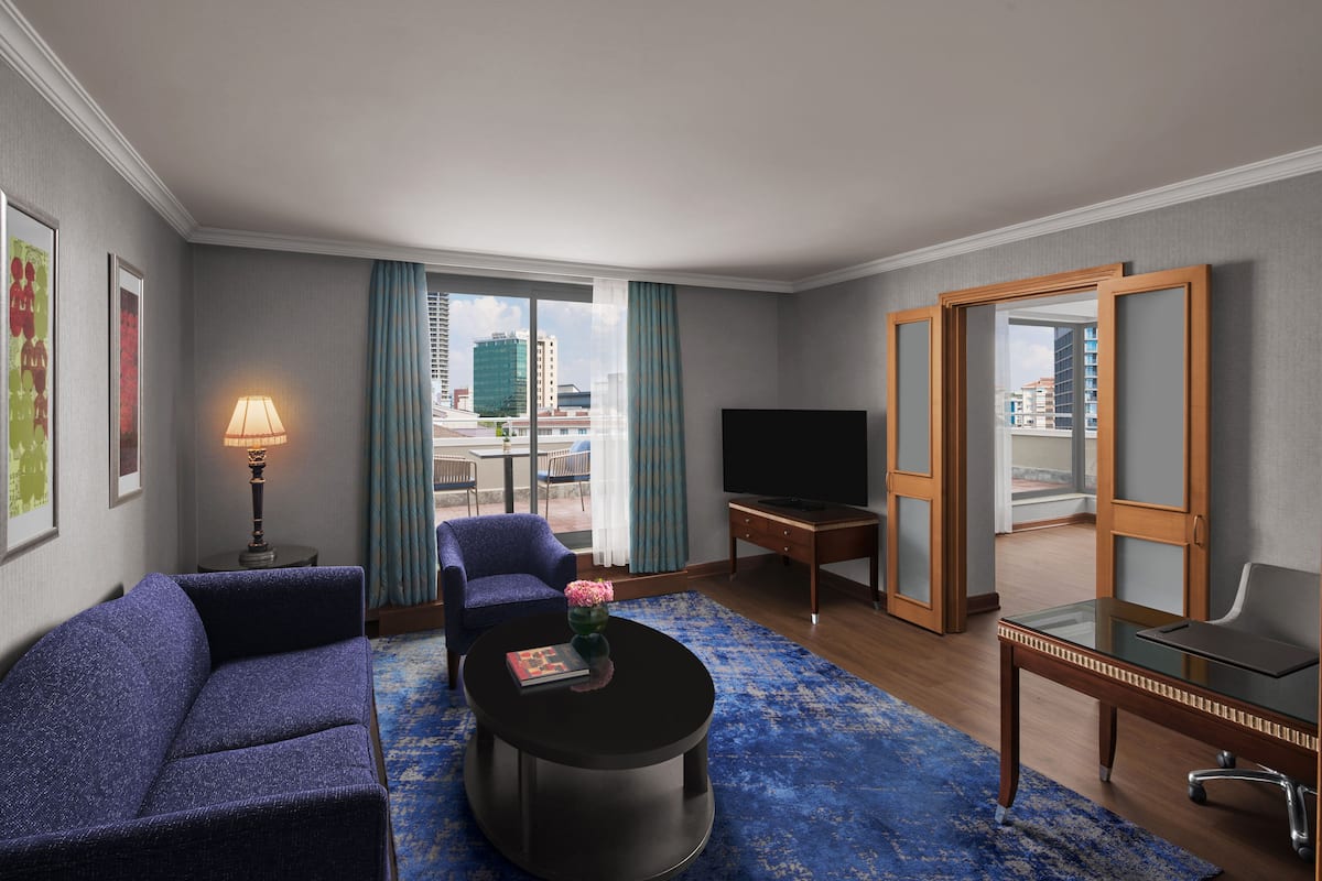 Habitación de hotel con sofá, sillón, mesa de centro, televisor y un espejo grande.