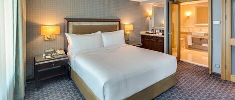 A hotel room with a large bed, bedside lamps, a nightstand, a bathroom with a mirror, and a patterned carpet.