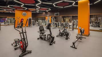 A gym with various exercise machines, mirrors, and orange accents.