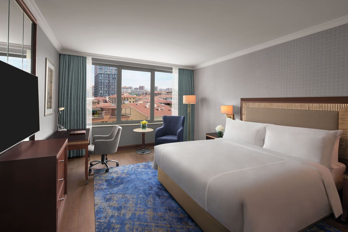 Una habitación de hotel con una cama grande, un escritorio, una silla, un televisor y vistas a la ciudad.
