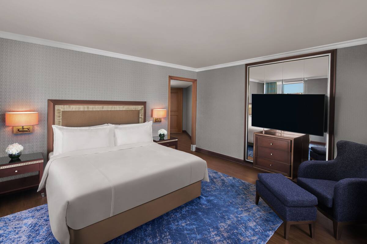 Una habitación de hotel con una cama grande, televisión, escritorio con lámpara y espejo.