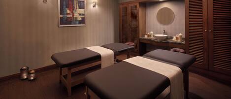 A spa room with two massage tables, a sink, and a mirror.