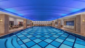 A large indoor swimming pool with a blue tiled floor, lounge chairs, and a ceiling with blue lighting. - Divan Ankara (Ankara)
