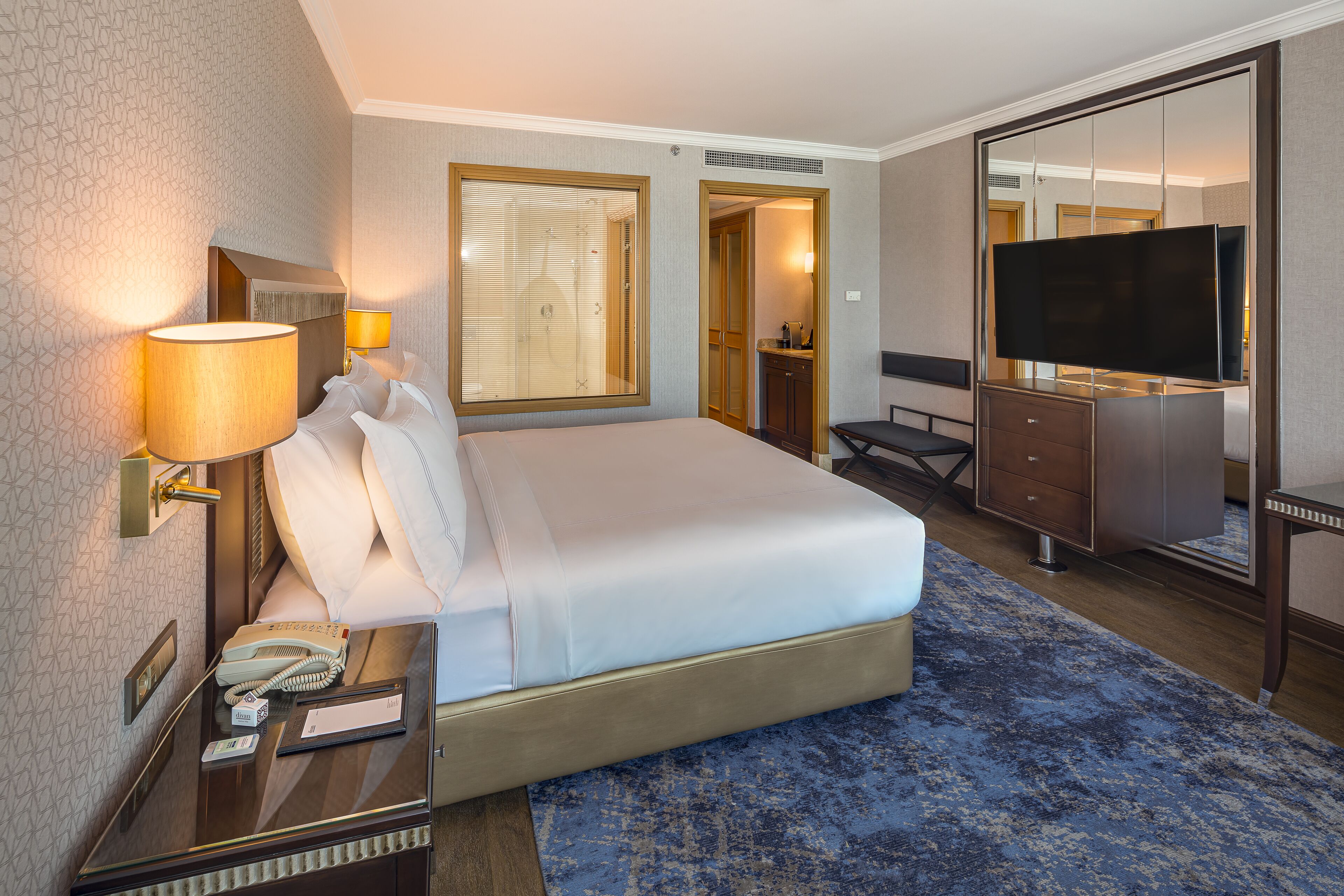 Une chambre d’hôtel avec un grand lit, un bureau avec une lampe, une télévision et une armoire.