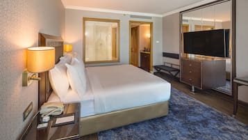 A hotel room with a large bed, a desk with a lamp, a TV, and a wardrobe.
