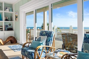 Quarto com vista para a praia, móveis de vime e uma estante de livros.