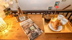 Et træbord med et magasin, en tepotte, et croissant og en bakke med kopper.