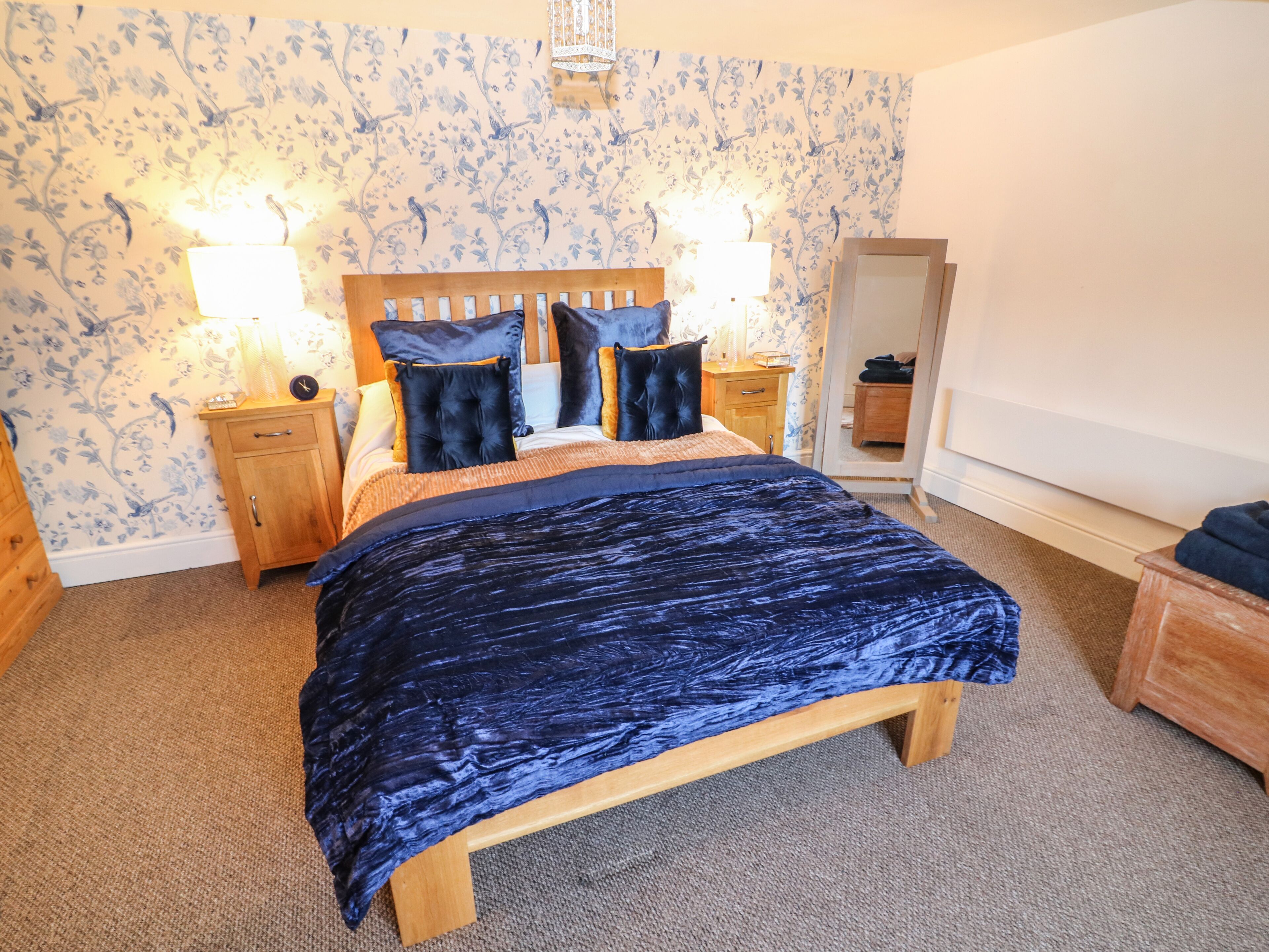 A bedroom with a large bed, wooden headboard, two bedside tables with lamps, and floral wallpaper.