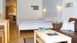Makuuhuoneessa on sänky, yöpöytä, ruskea nahkasohva, puinen pöytä ja taustalla näkyy keittiö.