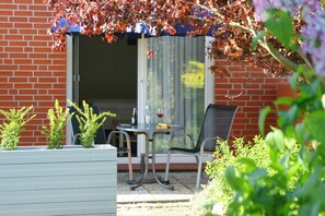 A patio with a table and chairs, a brick wall, and a window with a curtain.