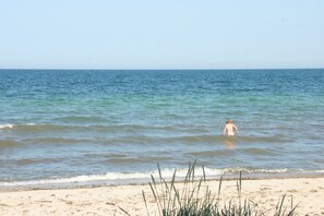 Una playa con una persona en el agua, cielo despejado y mar tranquilo.