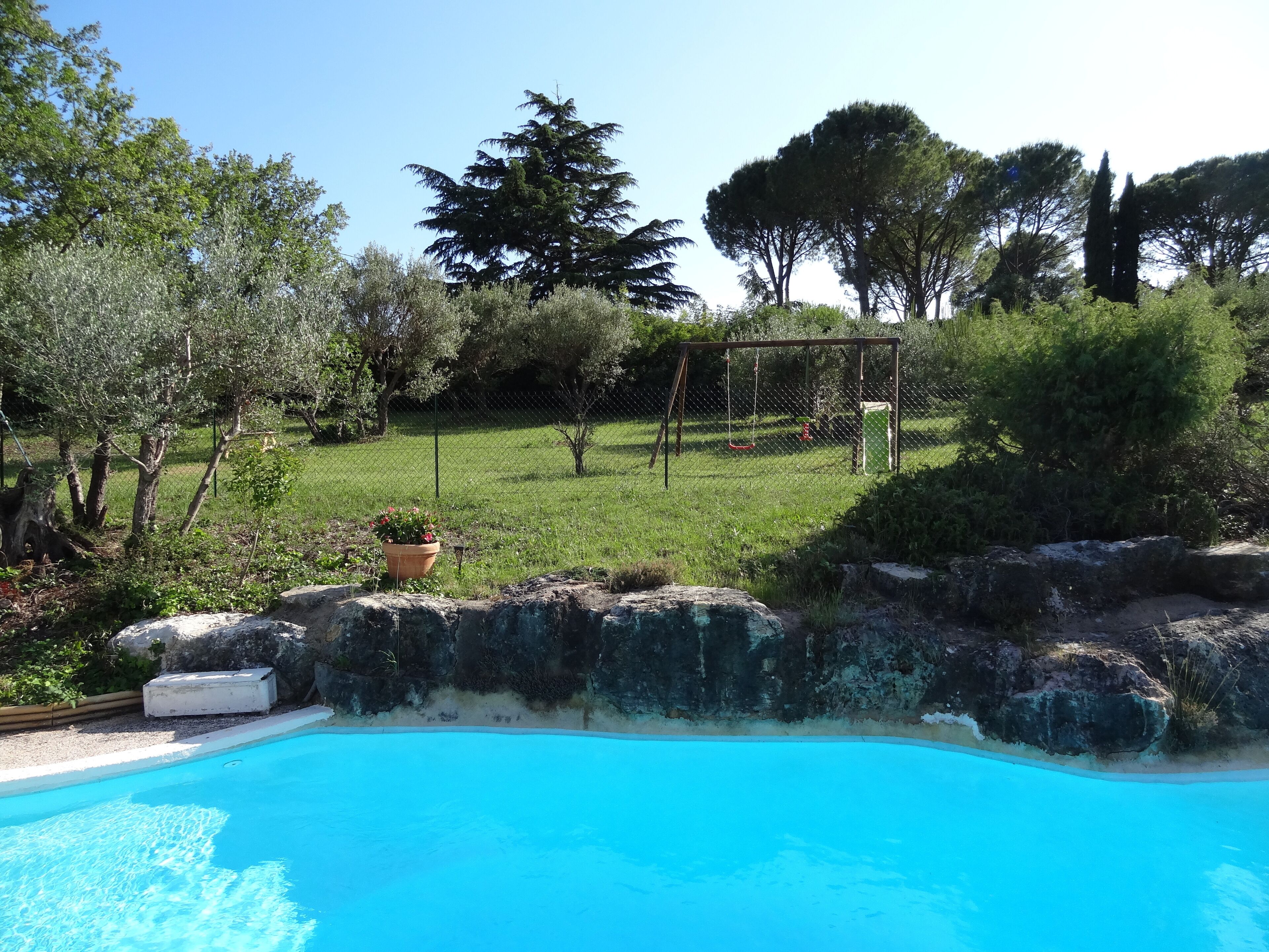 A swimming pool surrounded by a grassy area with trees and a swing set.