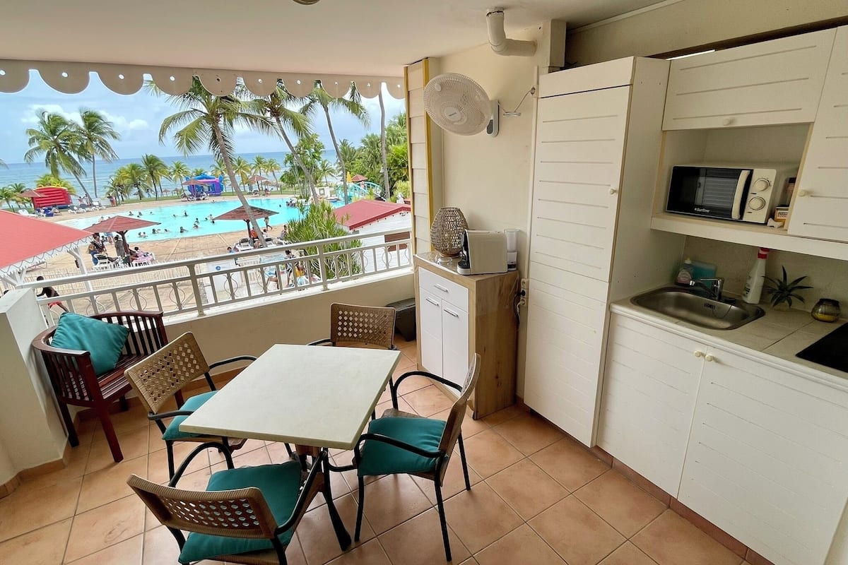 Ein Balkon mit Essbereich, eine Küche mit weißen Schränken, einer Mikrowelle und einem Spülbecken.