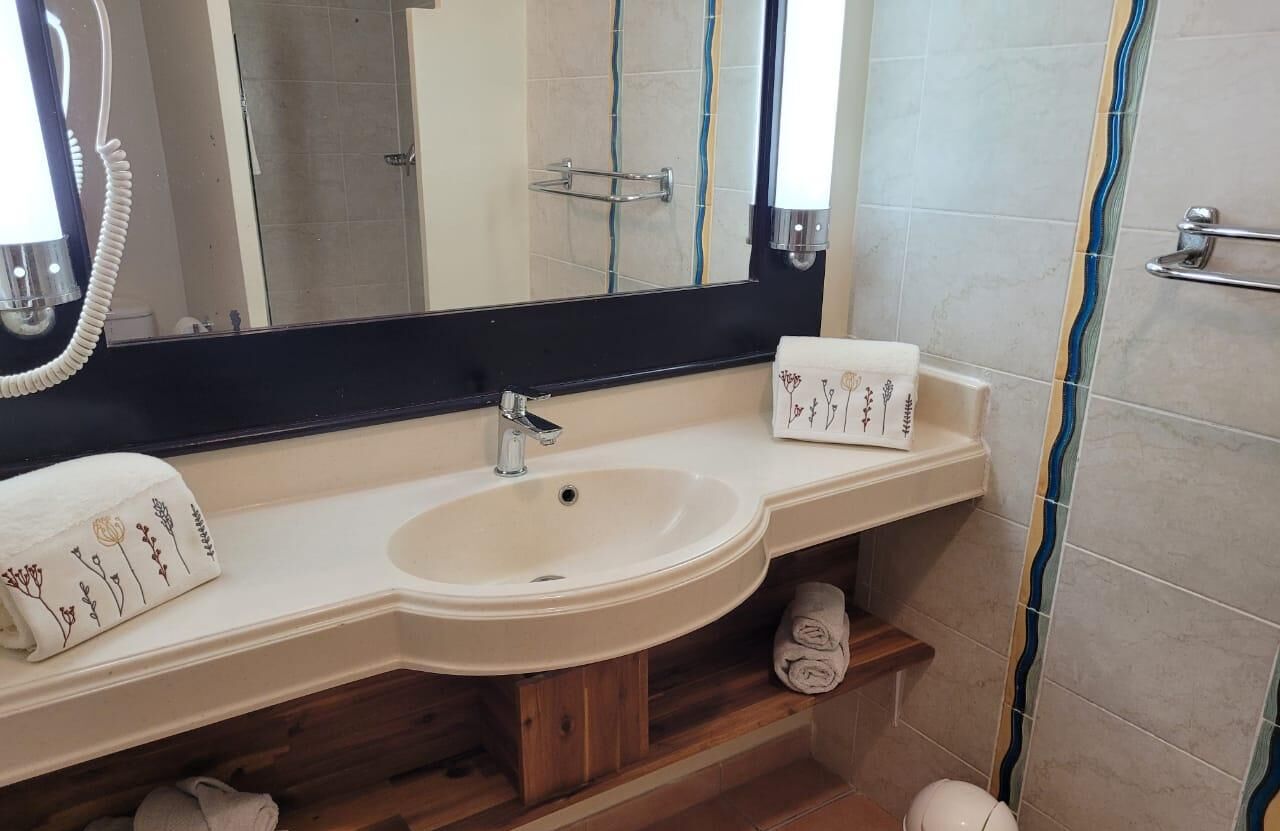 A bathroom with a white sink, a mirror, a towel rack, and a shower area.