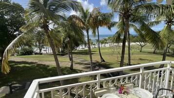 A balcony with a table set for two, overlooking a beach with palm trees and the ocean.