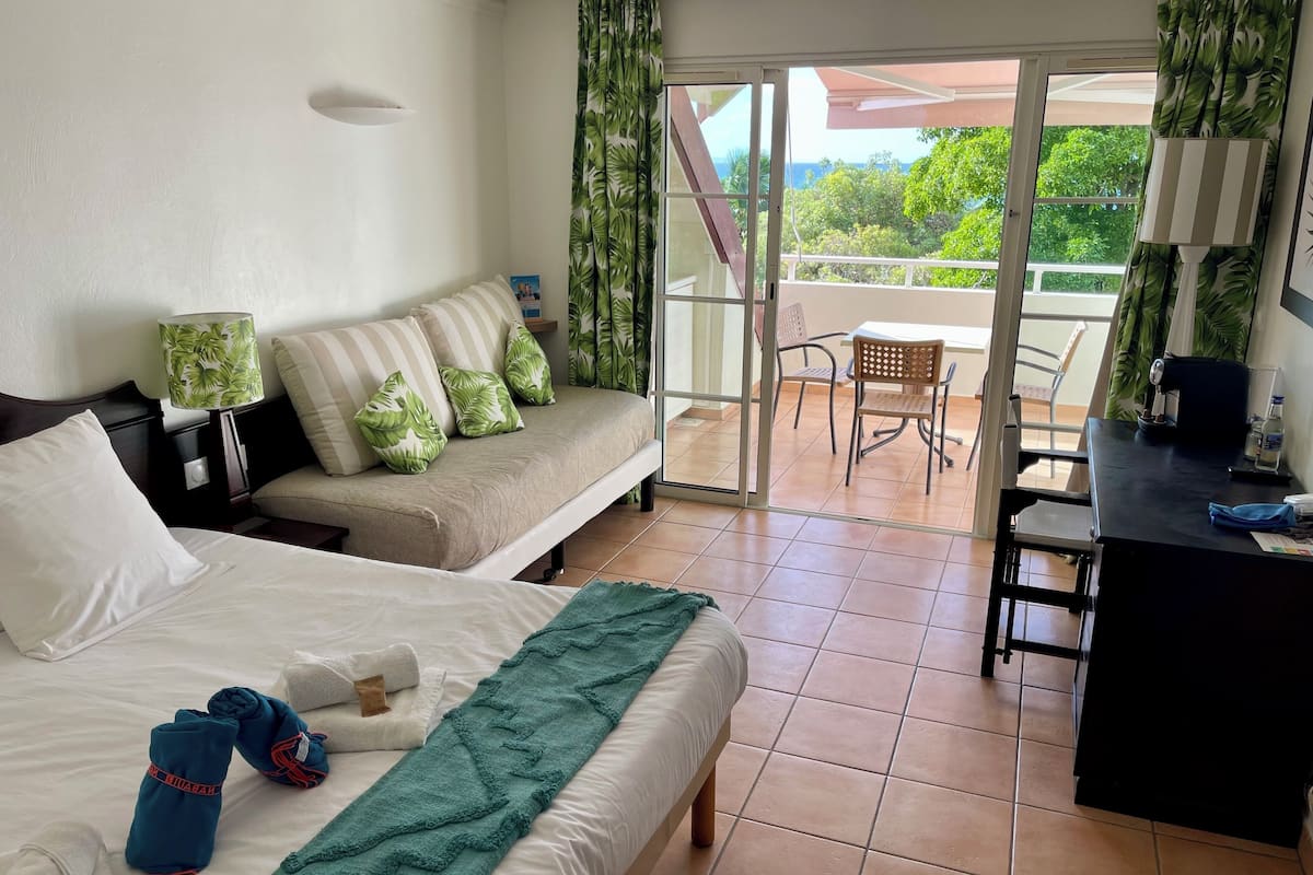 Ein Hotelzimmer mit Bett, Sofa, Schreibtisch und einem Balkon mit Blick.