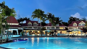 Een resort met een groot zwembad, palmbomen en een gebouw met een rood dak.
