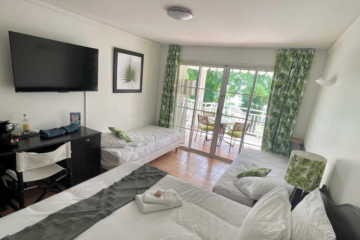 Ein Hotelzimmer mit Bett, Schreibtisch, Stuhl, Fernseher und einem Balkon mit Vorhängen.