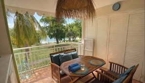 A balcony with a wooden table, chairs, and a thatched ceiling.