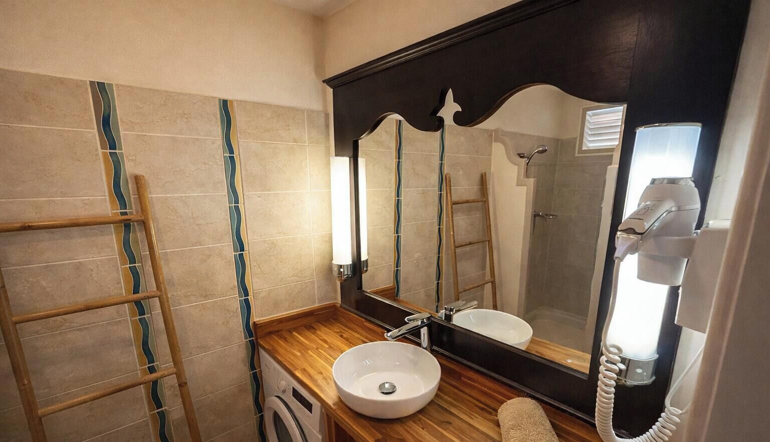 Un baño con tocador de madera, lavamanos, espejo, toalla y secador de pelo.