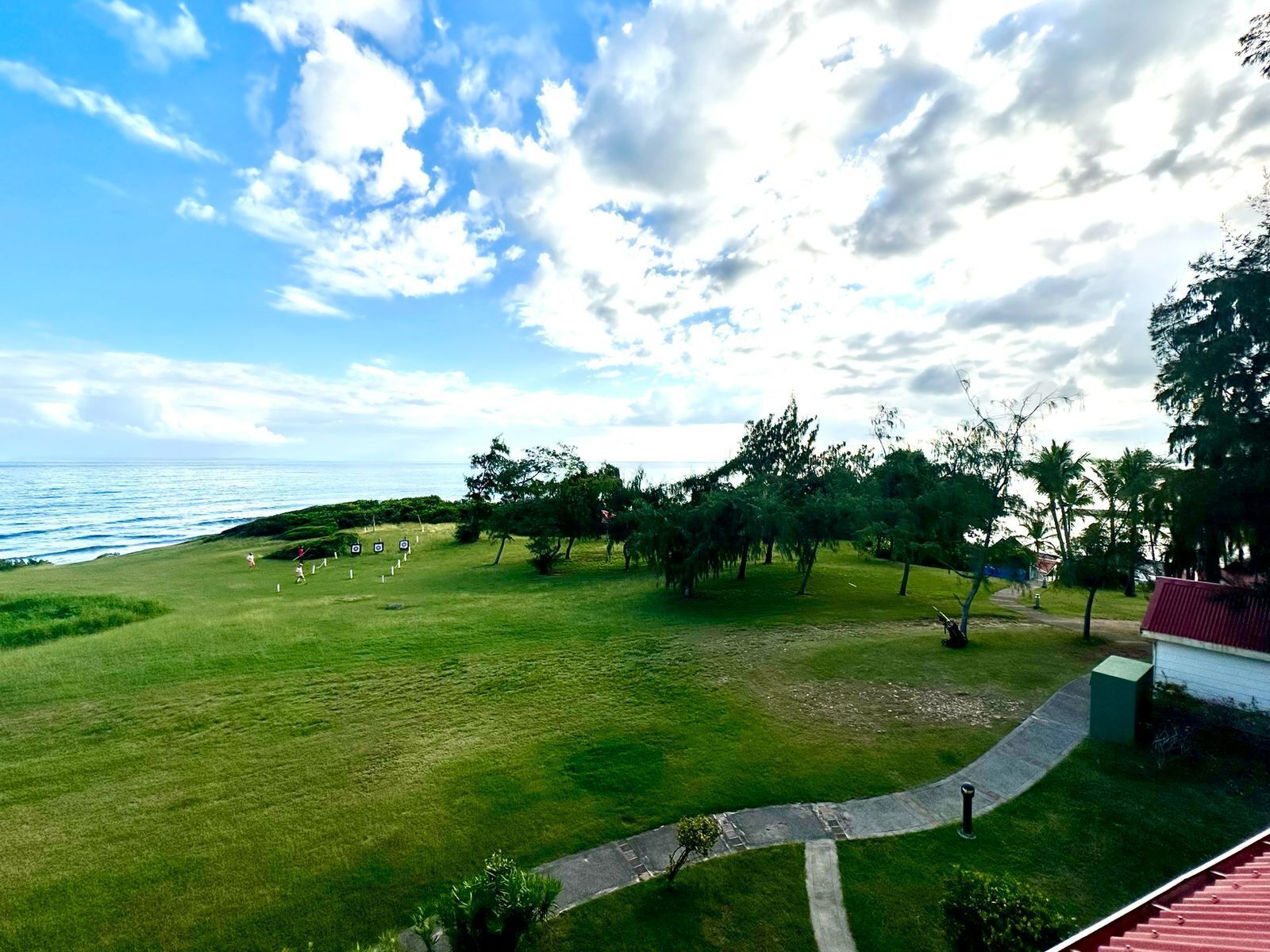 Un espacio verde con un sendero que lleva a un edificio, vistas al mar y árboles dispersos.
