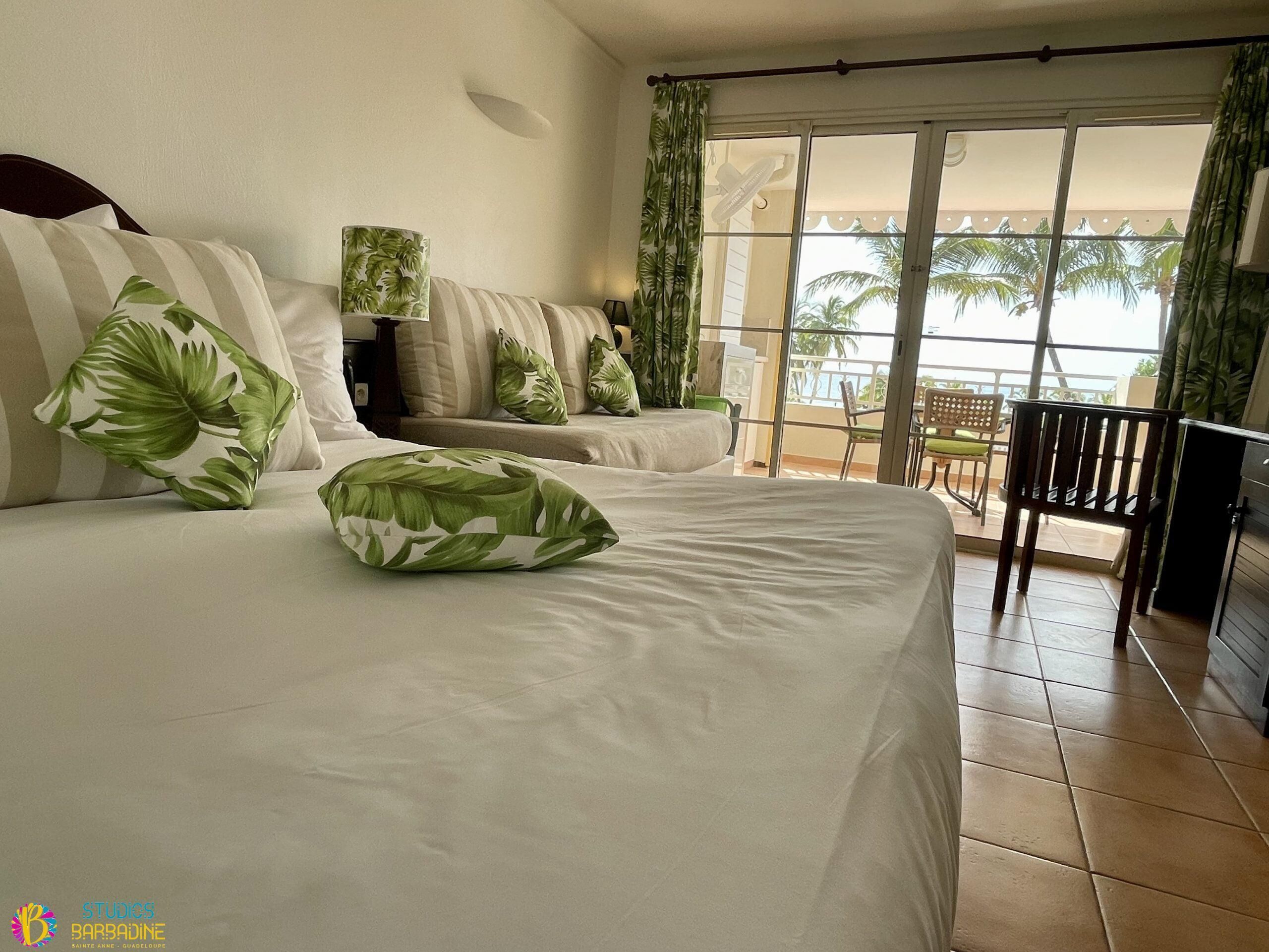 A hotel room with two beds, a balcony with a view of palm trees, and a chair.