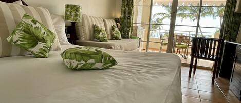 A hotel room with two beds, a balcony with a view of palm trees, and a chair.