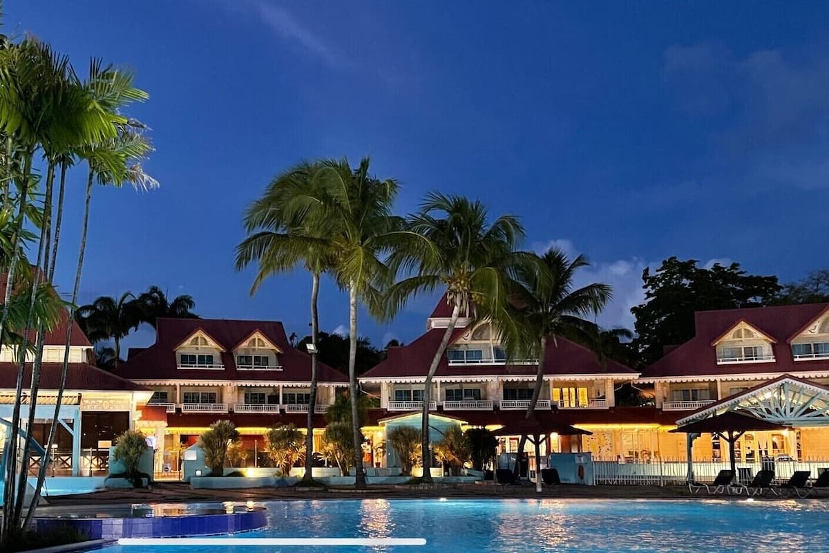 Ein Resort mit Swimmingpool, Palmen und einem großen Gebäude mit mehreren Balkonen.