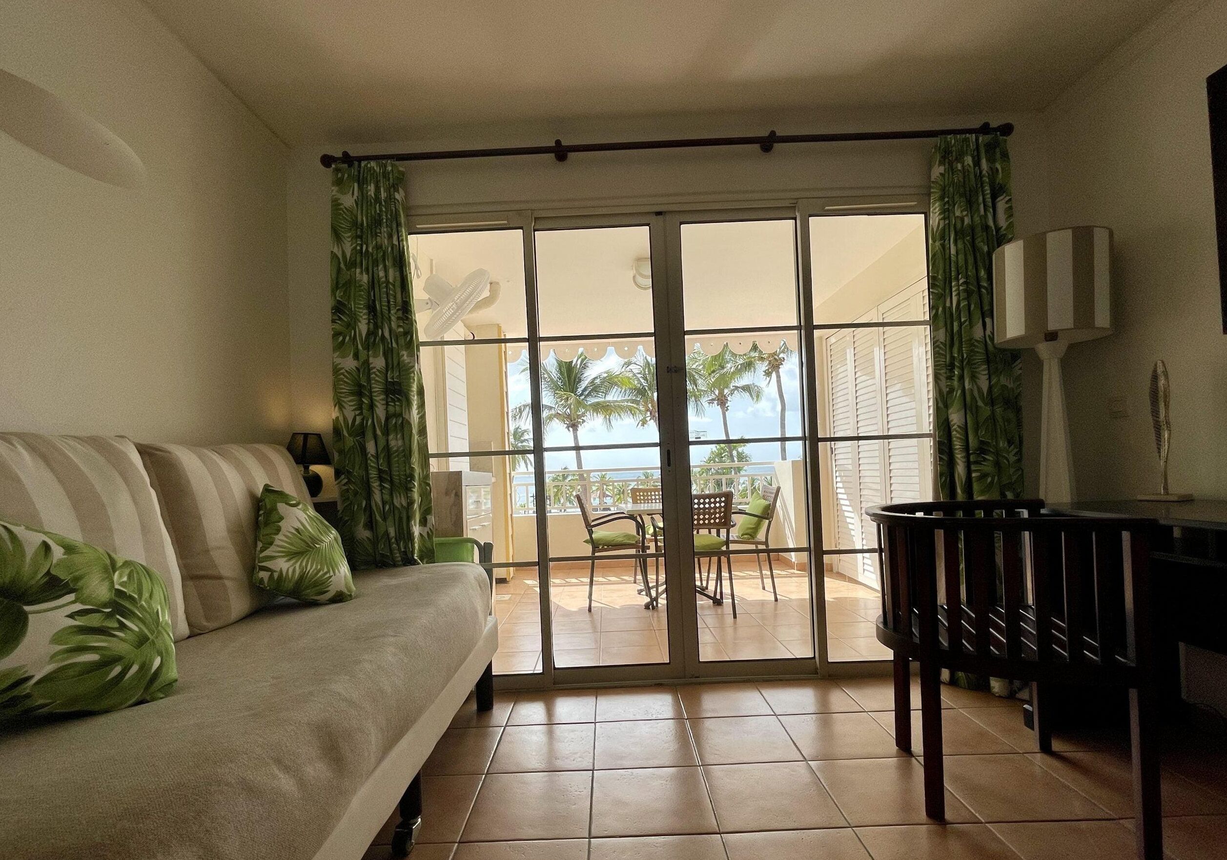 A living room with a sofa, a dining table, and a view of a balcony with chairs and a table.
